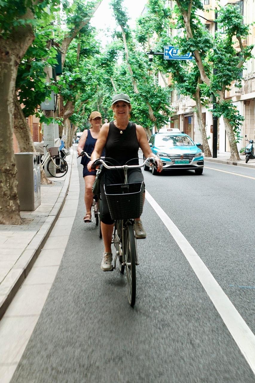 Two guests riding a tree lined Shanghai street on the Wheely bike tour